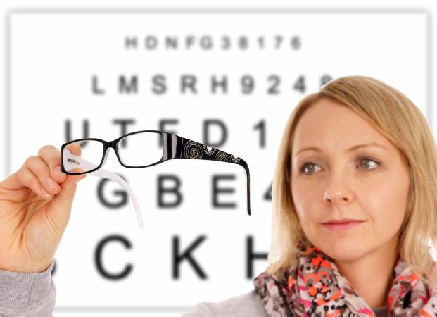 Woman holding spectacles in front of reading chart