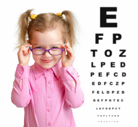 Child wearing spectacles in front of reading chart